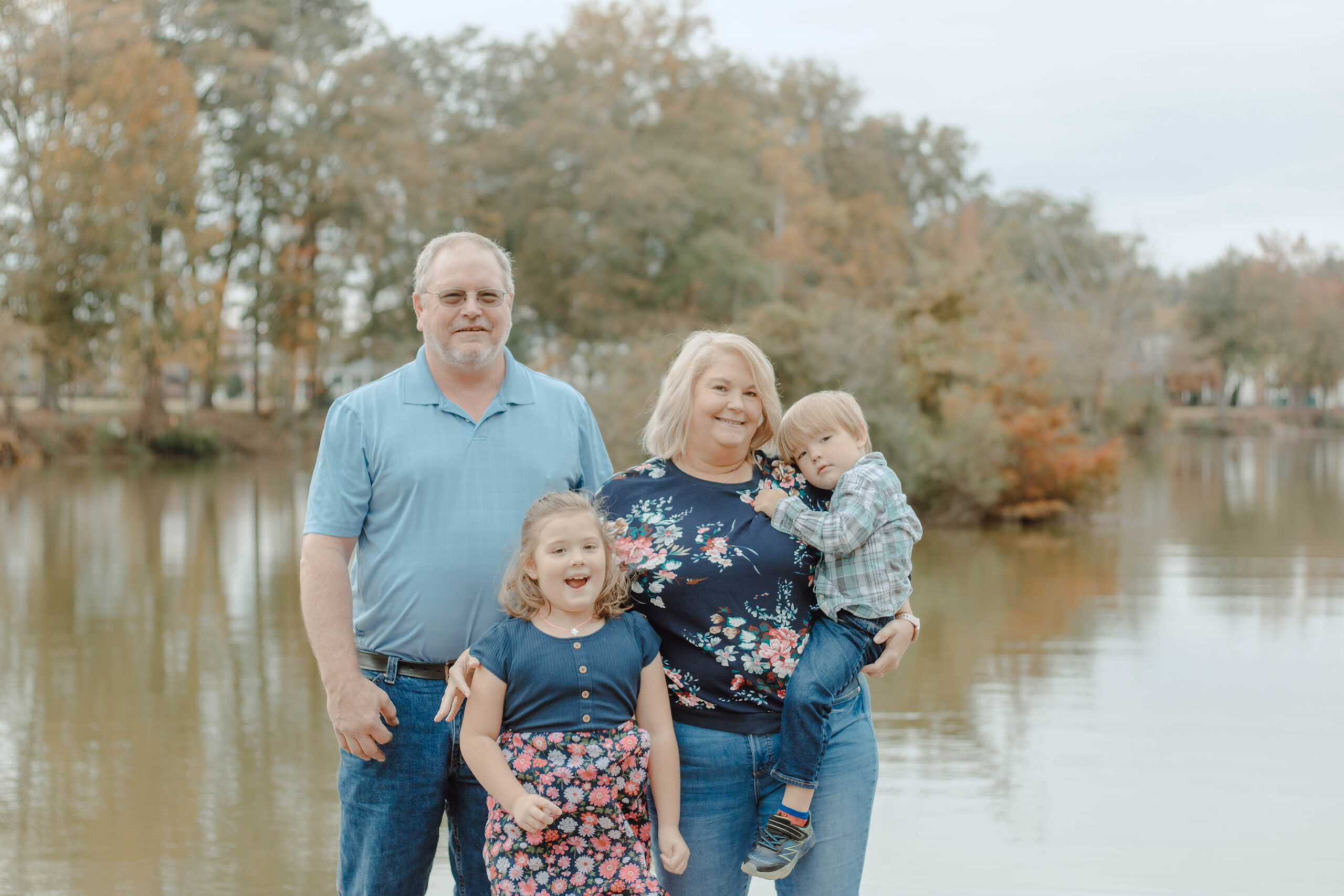 Grandparents stand with their grandchildren as everyone poses naturally in front of a beautiful pond