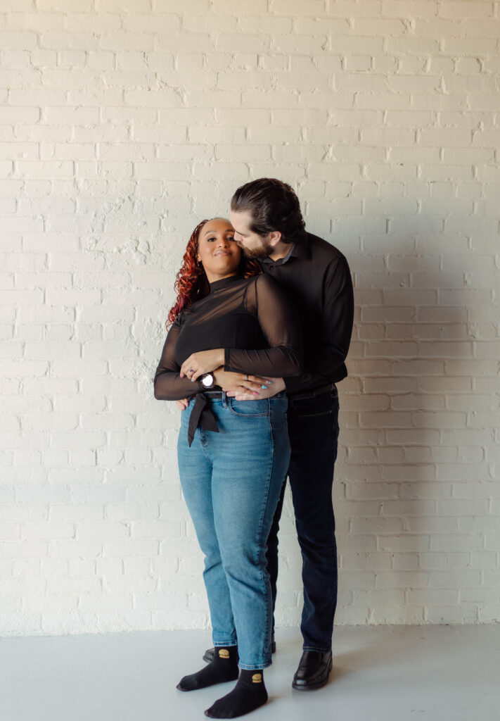 A man kisses his fiancée on her cheek during their studio engagement session in Augusta, Georgia
