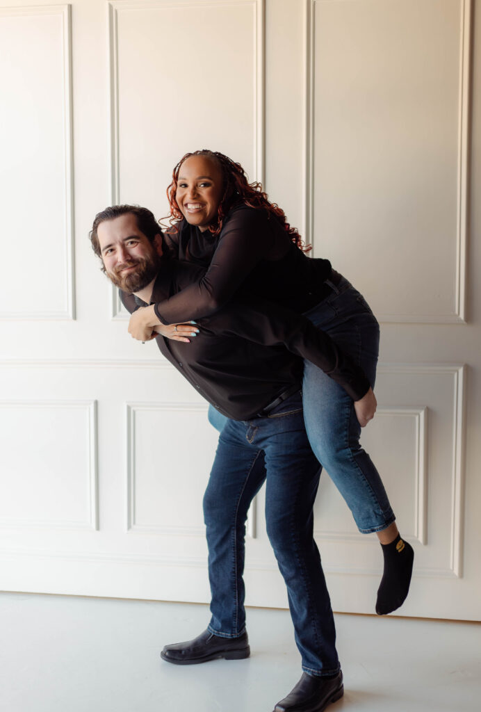 Engaged couple laughing during a piggyback pose at Opal Bay Studio in Augusta, Georgia