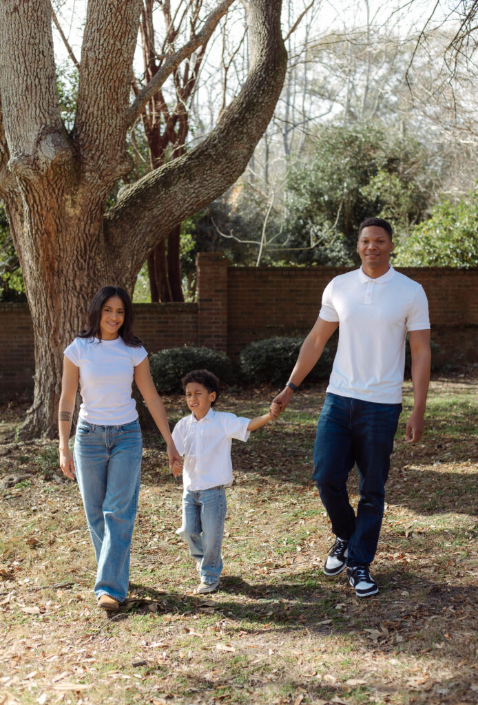 Family of three walking together through a sunny park in Augusta, Georgia during a lifestyle photo session