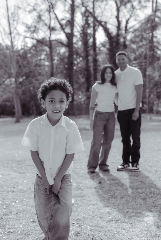 Little boy poses close to camera while parents watch in the background for photo session