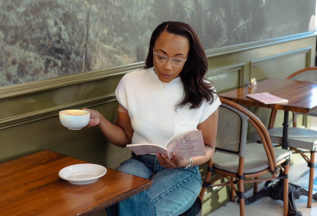 Author posing with a coffee and her book during a branding photoshoot at Rooted Coffeehouse
