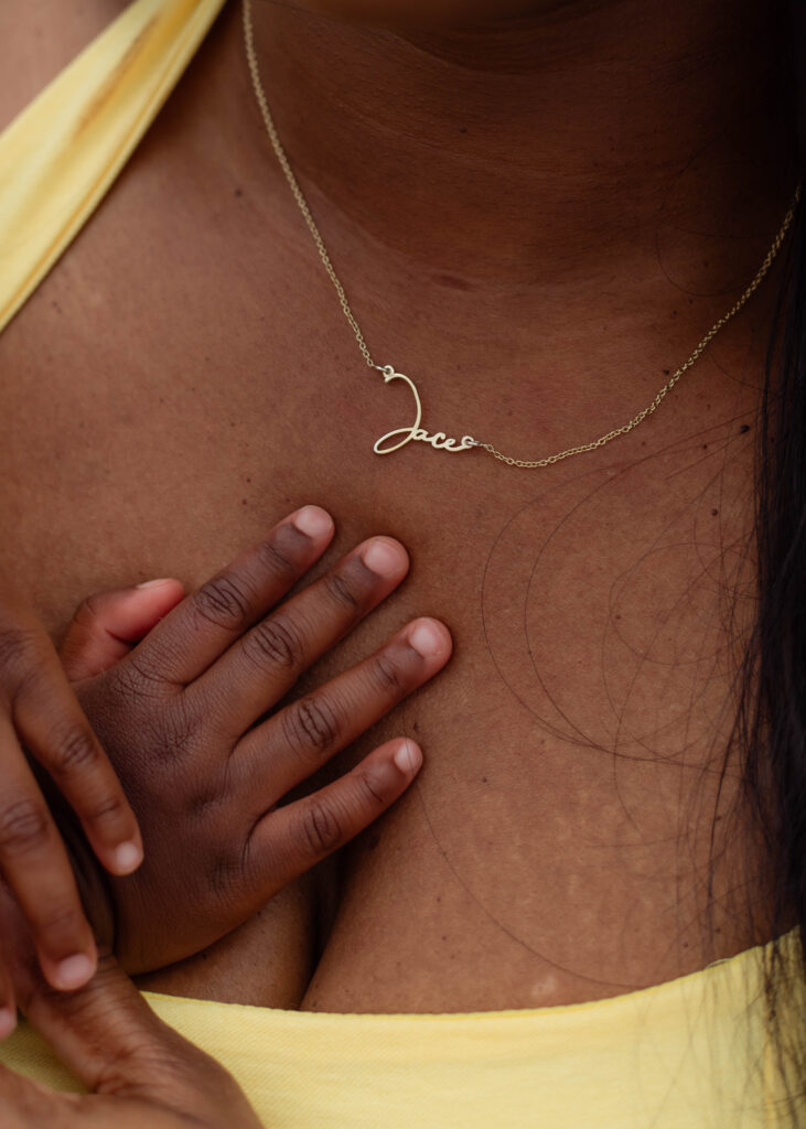 Close up of a baby's hand on his mother's chest with his name on her necklace