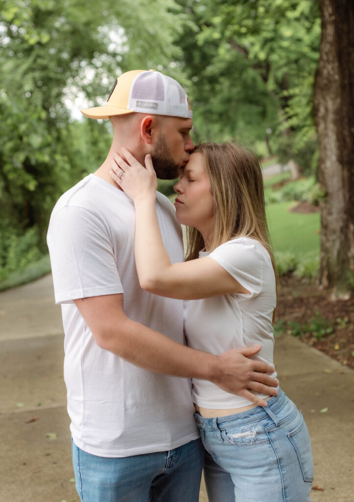 An engaged couple holding each other while he kisses her forehead