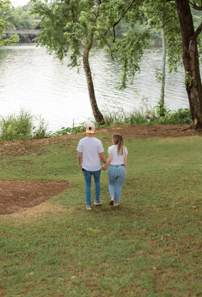 An engaged couple walking hand in hand towards the Savannah river