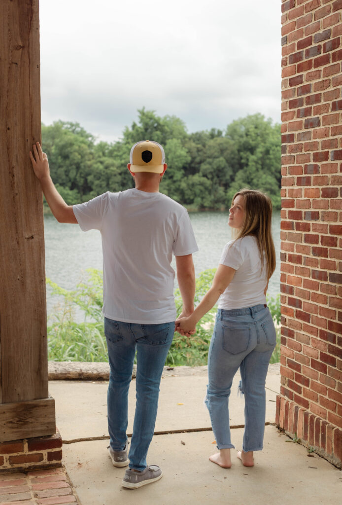 A man looks out at the river while his fiancée watches him with a smile