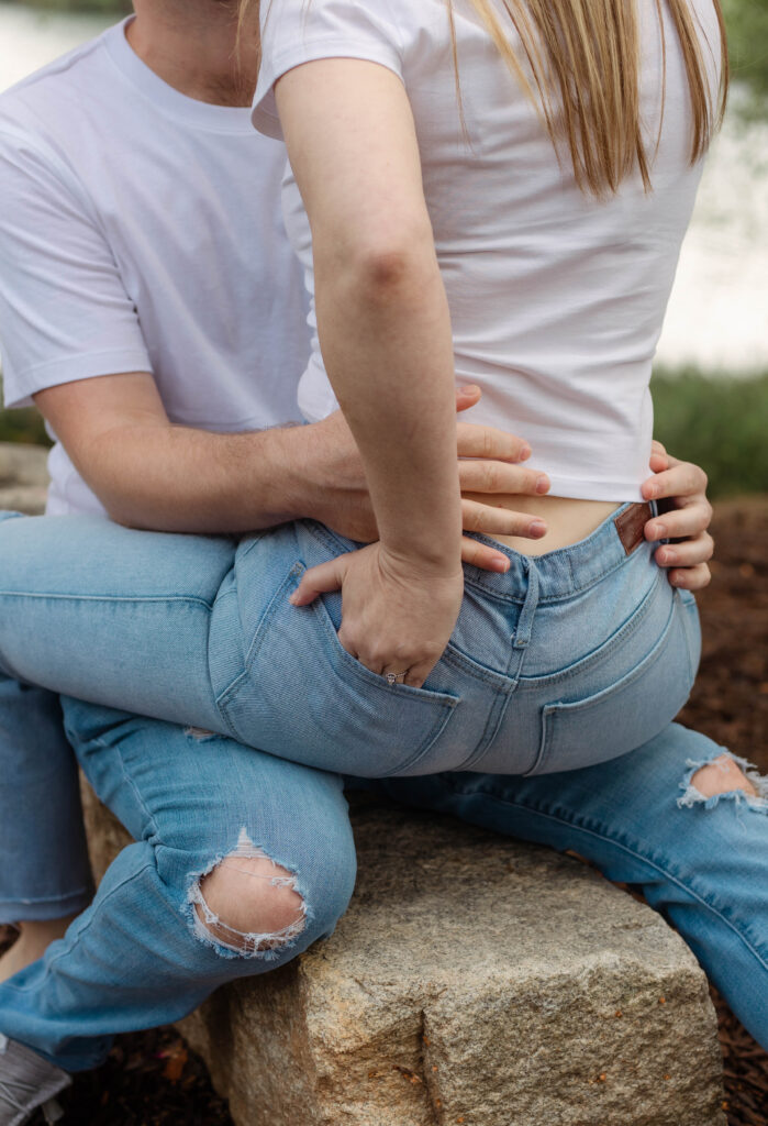Woman sits on fiancé's lap while showing her engagement ring with her hand in her pocket