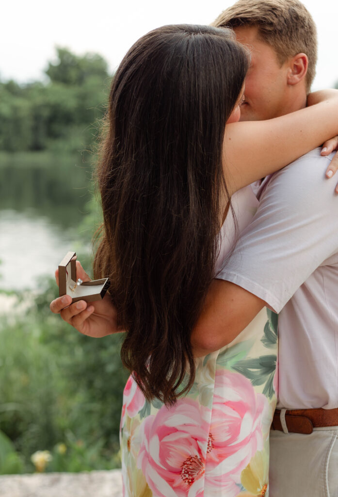 Couple hugs with the engagement ring behind the woman