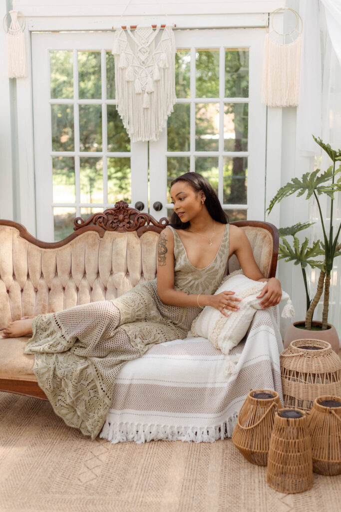 Woman laying on a vintage couch with boho decor and natural light streaming through the studio