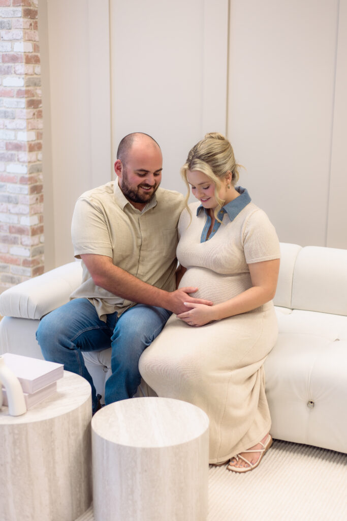 Couple holding pregnant belly for photo session while sitting on couch