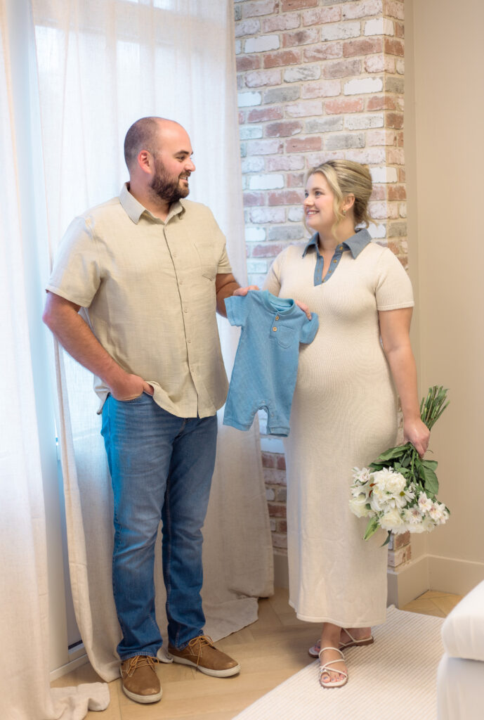 Expecting parents hold onto a blue onesie for photo session