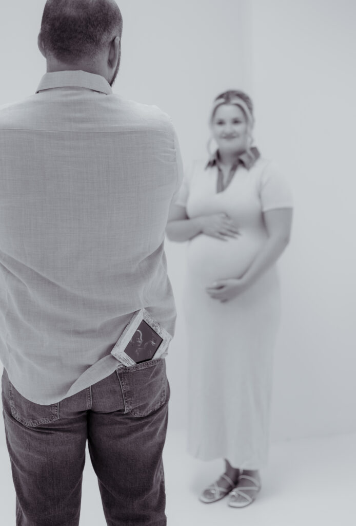 Black and white photo of a framed ultrasound in dad's pocket with expecting mom in the background