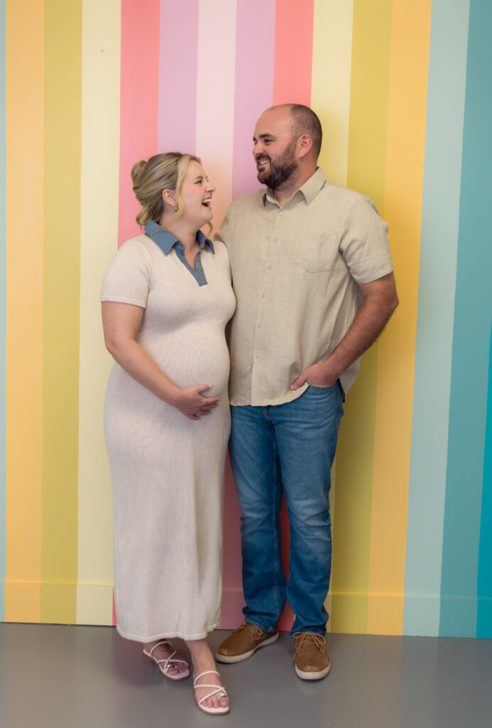 Couple stands in front of colorful striped wall to announce pregnancy