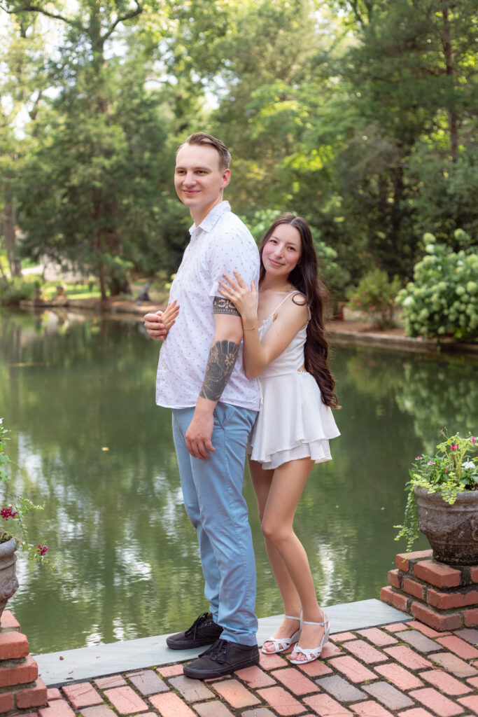Woman hugs her husband's back while they stand in front of a pond