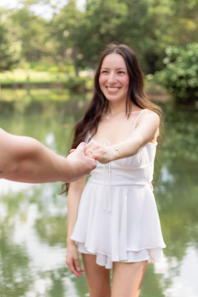 Woman smiles and holds her partner's hand while showing her ring