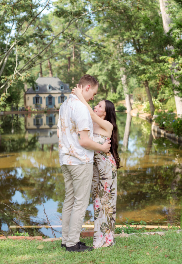 Couple holding each other close in front of historic house and pond