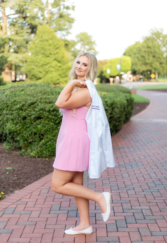 Grad posing with white coat draped over her shoulder with a smile