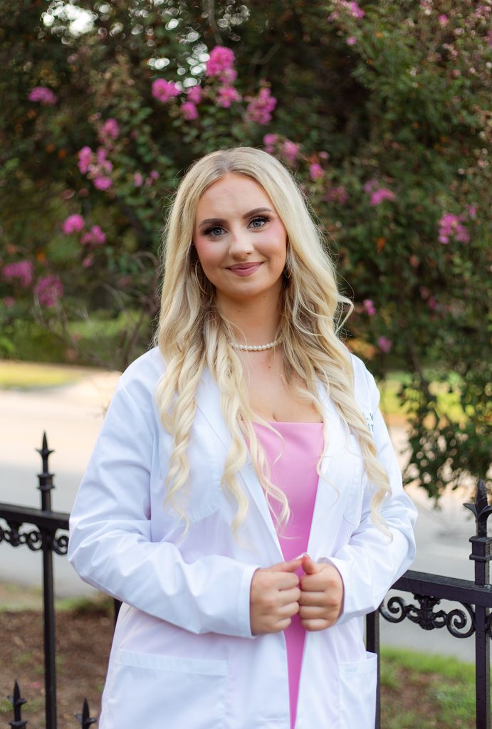 College grad poses professionally with white coat in front of pink flowers