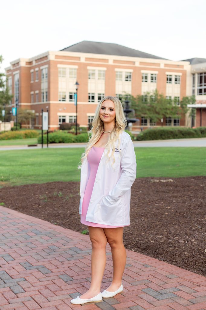 College grad posing with hands in pockets of white coat