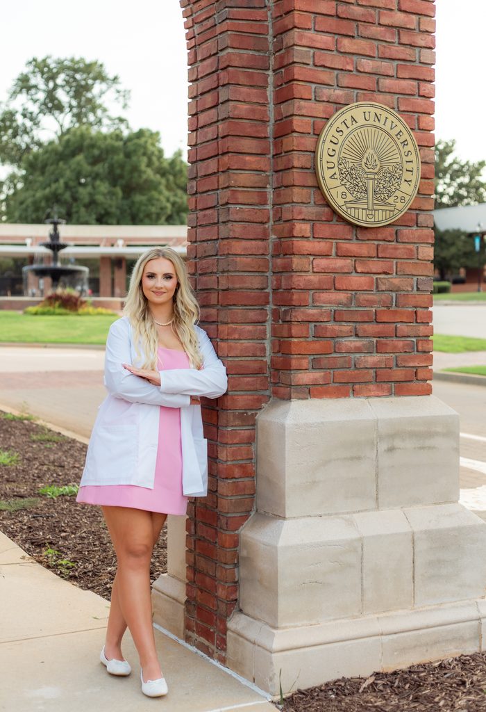 College grad posing near Augusta University sign at the Summerville campus