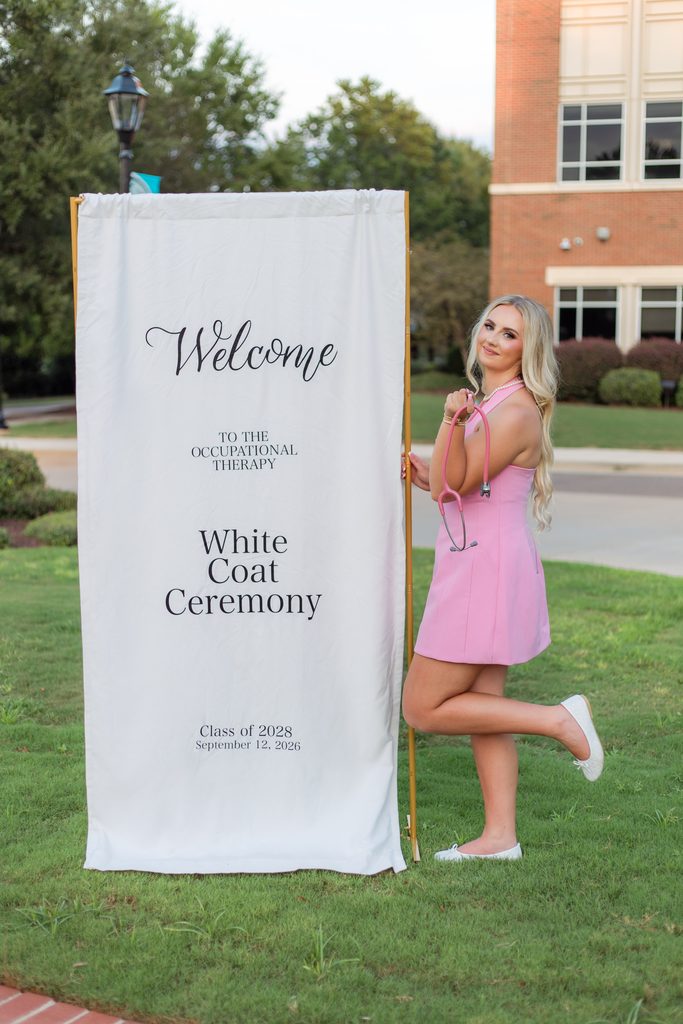 College grad posing near white coat ceremony sign