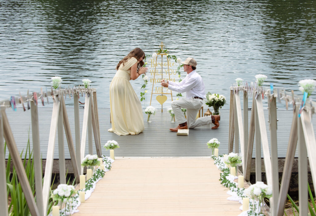 Man proposes on one knee to his girlfriend on a dock with decorations around