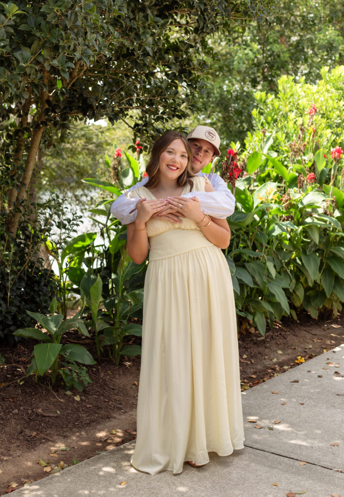 Man hugs fiancée from behind while the pose for the camera